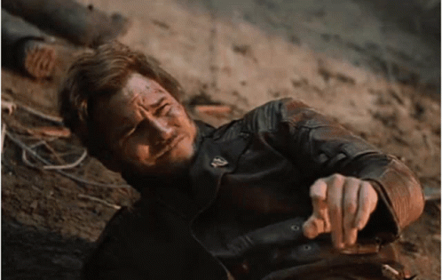 A Man In A Leather Jacket Is Laying On The Ground Pointing At The Camera GIF