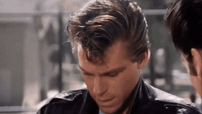 A Man In A Leather Jacket Is Looking Down At Something While Another Man Looks On . GIF