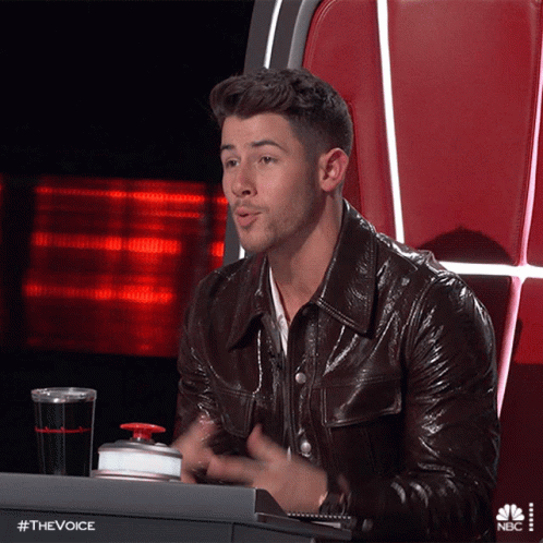 A Man In A Leather Jacket Is Sitting At A Desk With A Nbc Logo On The Bottom GIF