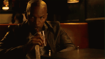 A Man In A Leather Jacket Is Sitting At A Table Drinking A Drink . GIF