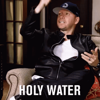 A Man In A Leather Jacket Is Sitting In A Chair With The Words Holy Water On The Bottom GIF