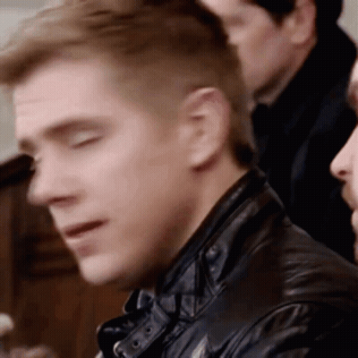 A Man In A Leather Jacket Is Sitting In A Row Of People . GIF