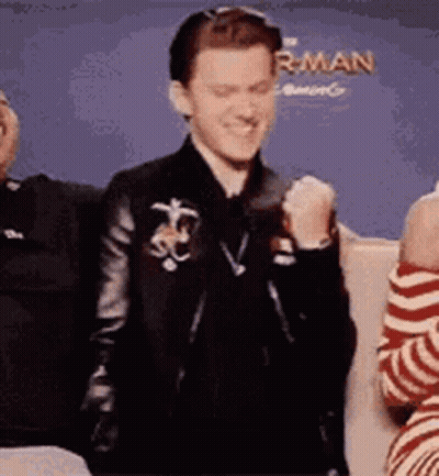 A Man In A Leather Jacket Is Sitting Next To A Woman In A Striped Shirt And Making A Fist . GIF
