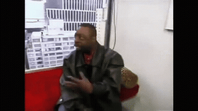 A Man In A Leather Jacket Is Sitting On A Red Couch And Talking On A Cell Phone . GIF
