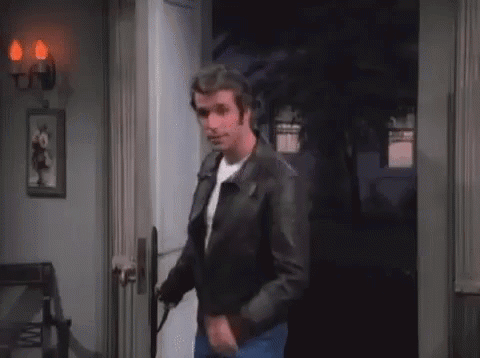 A Man In A Leather Jacket Is Standing In A Doorway With The Letter A Written On His Chest . GIF