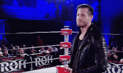 A Man In A Leather Jacket Is Standing In A Wrestling Ring With A Sign That Says Rqf GIF