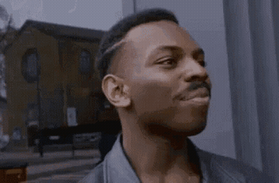 A Man In A Leather Jacket Is Standing In Front Of A Building And Making A Funny Face . GIF