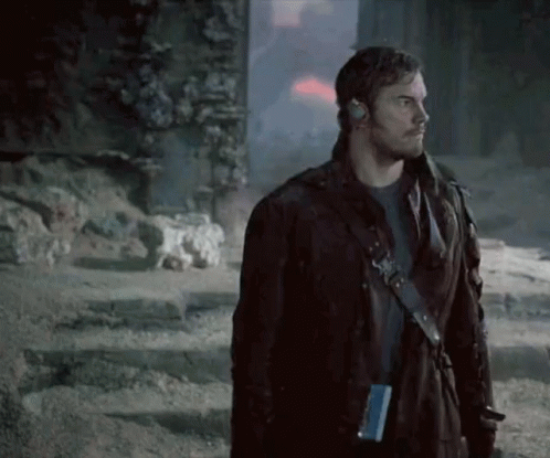 A Man In A Leather Jacket Is Standing In Front Of A Building In A Dark Room . GIF