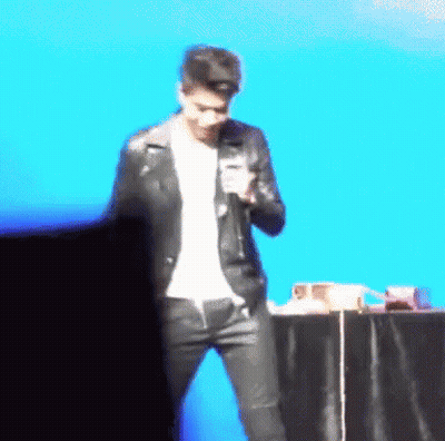 A Man In A Leather Jacket Is Standing In Front Of A Microphone GIF