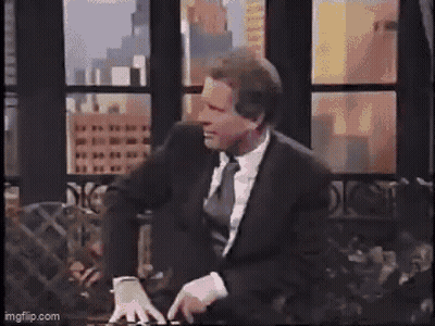 A Man In A Leather Jacket Is Standing In Front Of A Window In A Living Room . GIF