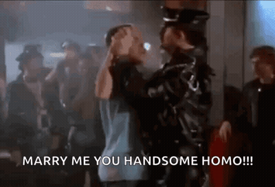 A Man In A Leather Jacket Is Standing Next To A Man In A Blue Shirt In A Crowd Of People . GIF