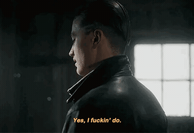 A Man In A Leather Jacket Is Talking To Another Man In A Dark Room . GIF