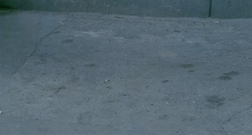 A Man In A Leather Jacket Is Walking Down A Narrow Street GIF