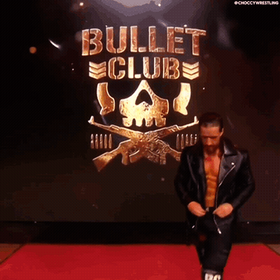 A Man In A Leather Jacket Is Walking Down A Red Carpet In Front Of A Bullet Club Logo GIF