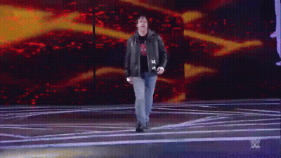 A Man In A Leather Jacket Is Walking On A Stage In Front Of A Wwe Logo GIF