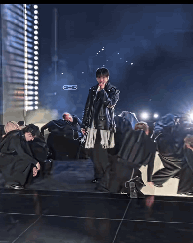 A Man In A Leather Jacket Sings Into A Microphone In Front Of A Crowd GIF
