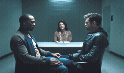 A Man In A Leather Jacket Sits In A Chair Talking To Two Other Men GIF