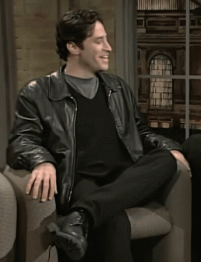 A Man In A Leather Jacket Sits In A Chair GIF