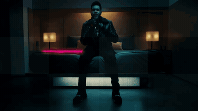 A Man In A Leather Jacket Sits On A Bed GIF