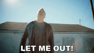 A Man In A Leather Jacket Stands In Front Of A Building With The Words Let Me Out GIF