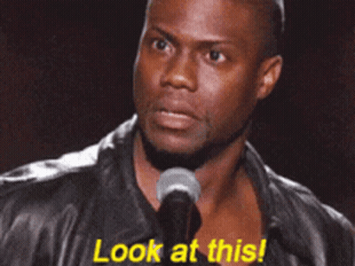 A Man In A Leather Jacket Stands In Front Of A Microphone And Says " Look At This " GIF