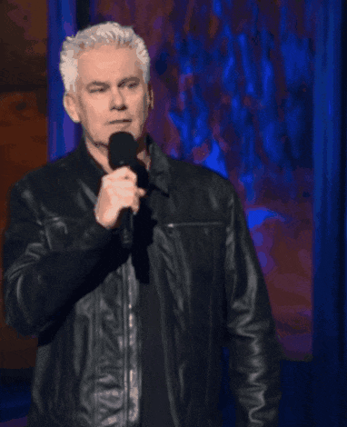 A Man In A Leather Jacket Stands In Front Of A Microphone With The Words Get A Dictionary Above Him GIF