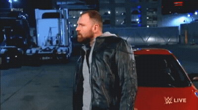 A Man In A Leather Jacket Stands In Front Of A Red Car With Fire Coming Out Of It And The Words Raw On The Bottom GIF