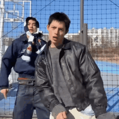A Man In A Leather Jacket Stands Next To Another Man In A Scarf GIF