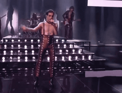 A Man In A Leather Outfit Is Singing Into A Microphone On Stage . GIF