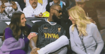 A Man In A Lebron James Jersey Is Sitting In A Stadium With Two Women . GIF