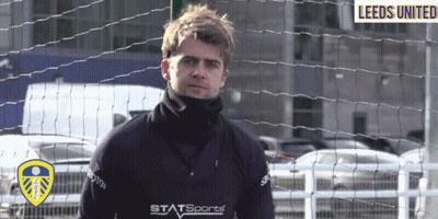 A Man In A Leeds United Jersey Stands Behind A Fence GIF