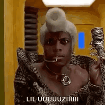 A Man In A Leopard Print Coat Is Holding A Cane In His Hand And Talking On A Cell Phone . GIF