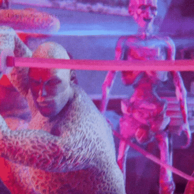 A Man In A Leopard Print Costume Is Standing Next To A Statue Of A Man With A Sword . GIF