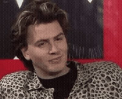 A Man In A Leopard Print Shirt Is Sitting On A Red Couch And Making A Funny Face . GIF