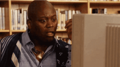 A Man In A Library Looking At A Computer Monitor GIF