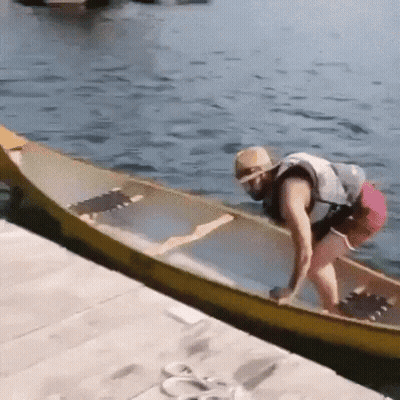 A Man In A Life Jacket Is Pushing A Yellow Canoe Into The Water . GIF
