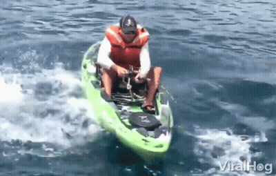 A Man In A Life Jacket Is Riding A Green Kayak On A Lake GIF