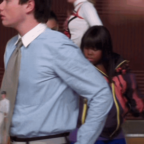 A Man In A Light Blue Shirt And Tie Stands Next To A Woman In A Pink Jacket GIF