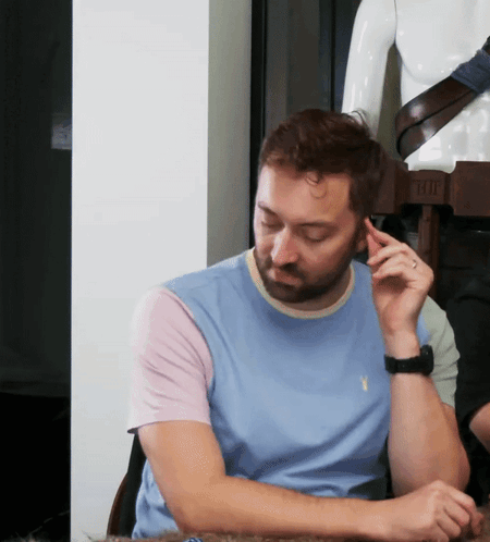 A Man In A Light Blue Shirt Is Sitting In Front Of A Mannequin With A Belt That Says T-Shirt GIF