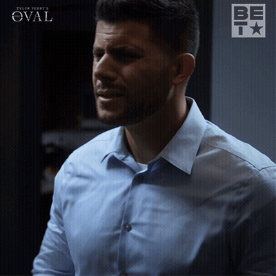 A Man In A Light Blue Shirt Is Standing In Front Of A Sign That Says Tyler Perry 'S Oval GIF