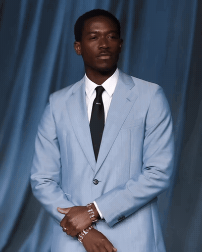 A Man In A Light Blue Suit And Black Tie Has A Bracelet On His Wrist GIF