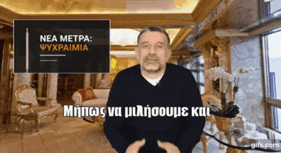 A Man In A Living Room With A Sign That Says " Nea Metpa " GIF