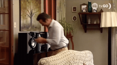 A Man In A Living Room With A Tvgo Logo On The Wall GIF