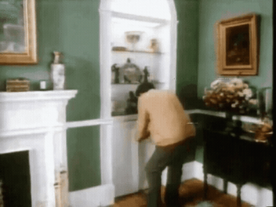 A Man In A Living Room With Green Walls And A Fireplace GIF
