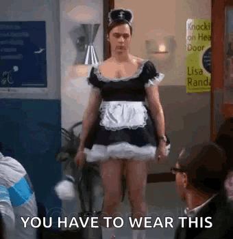 A Man In A Maid Costume Is Standing In A Room With People . GIF