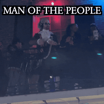 A Man In A Man Of The People Costume Stands In Front Of A Green Light GIF