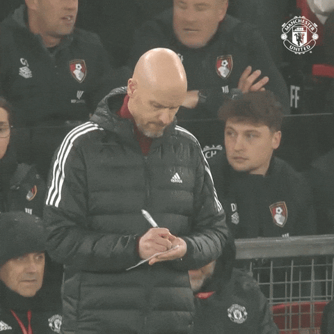 A Man In A Manchester United Jacket Writes On A Piece Of Paper With A Pen GIF