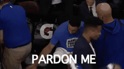 A Man In A March For Our Lives Shirt Is Sitting In A Chair With A Group Of People Surrounding Him . GIF