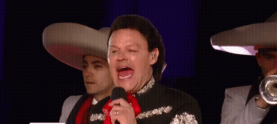 A Man In A Mariachi Outfit Is Singing Into A Microphone While Two Men Play Trumpets In The Background GIF