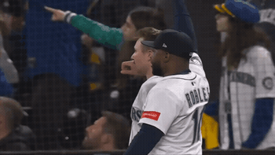 A Man In A Mariners Jersey Stands With Another Man GIF